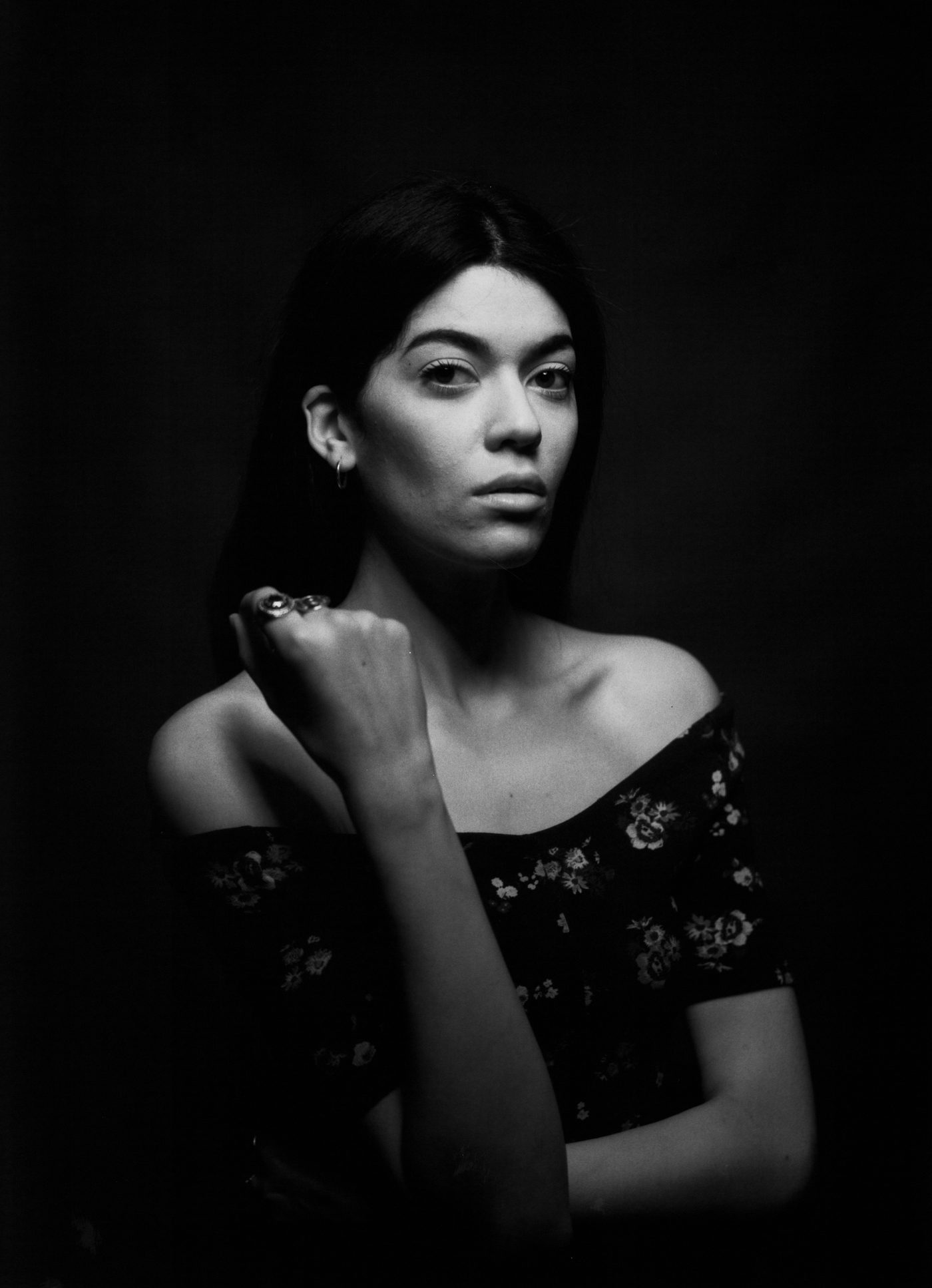 Black-and-white studio portrait of a woman with dark hair, one hand raised to her shoulder